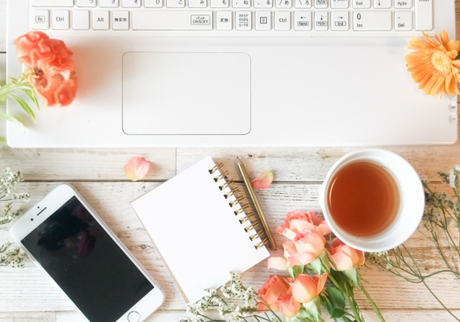 パソコンとスマホ、メモ、紅茶、お花が並んでいる画像